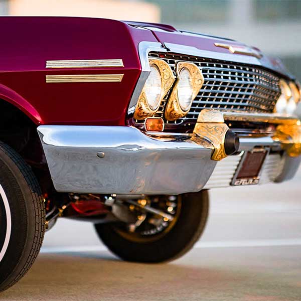 close up of the front of a crimson red lowrider car with gold rims
