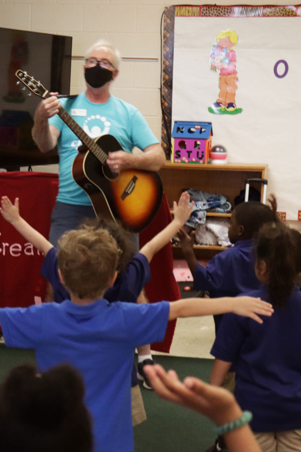 musician Mr. Freddy playing an acoustic guitar in front of dancing children in a class room 
