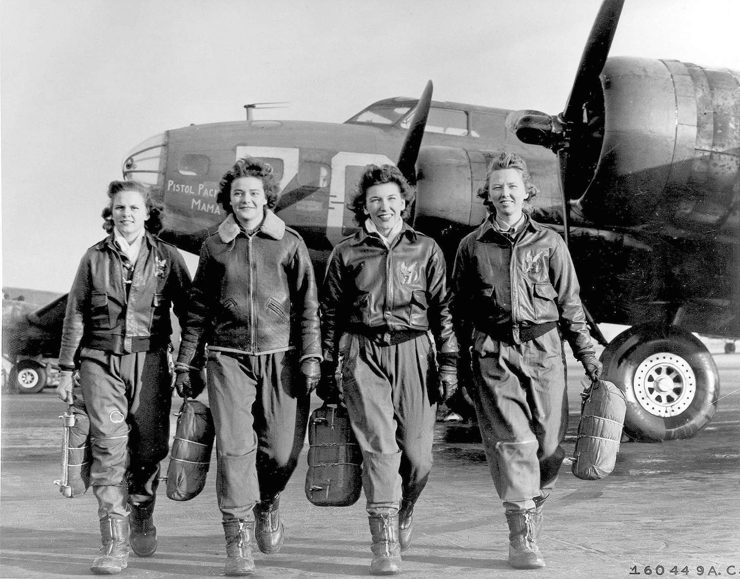 Four WASP pilots in flight gear and carrying parachutes with airplane in background
