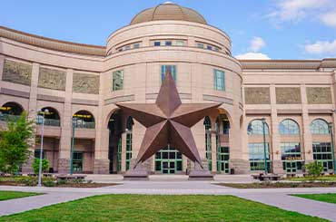 exterior of the Bullock Museum that has a large dome and a bronze Lone Star Statue on the plaza