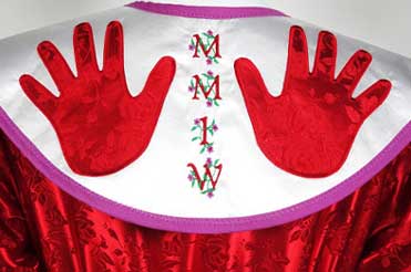 close up of red jingle dress showing two bright red hands on a white yoke with the letters MMIW embroidered down the center
