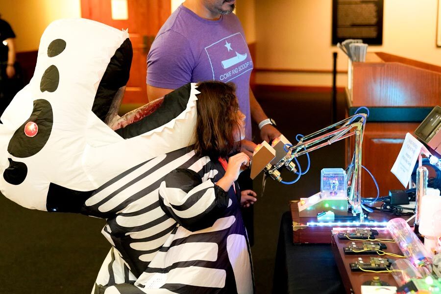 child dressed up in an inflatable dinosaur costume interacts with circuit boards on a table