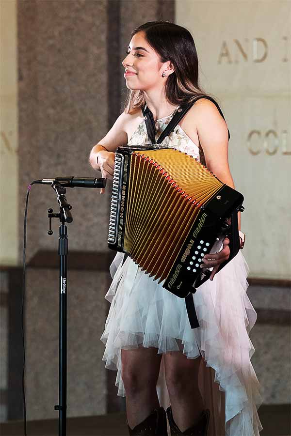 woman standing at a microphone smiling playing the accordion