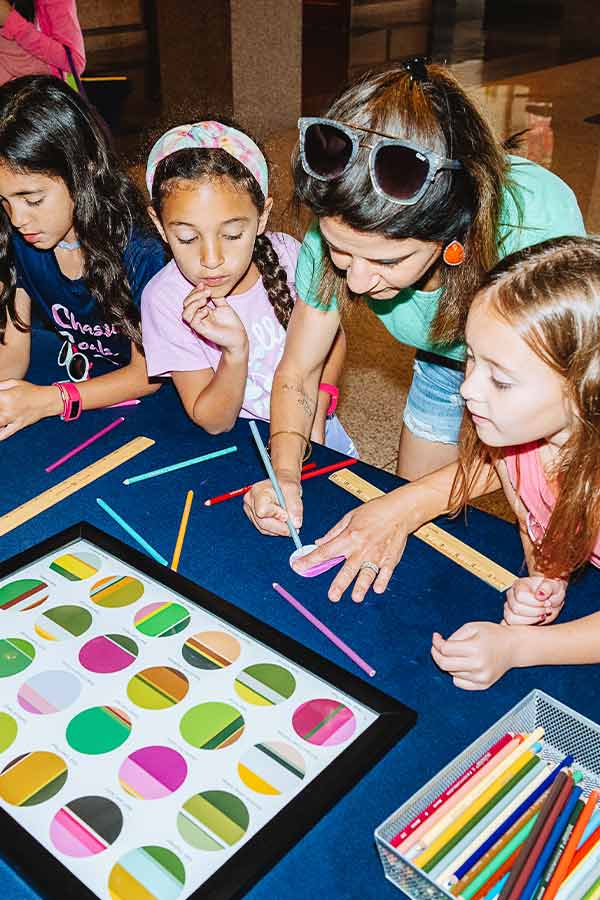 one adult and two children doing a coloring project at a table