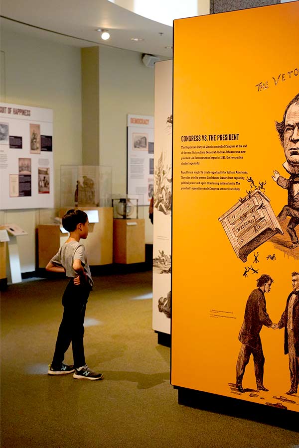 child standing in front of an orange wall graphics in the Bullock Museum exhibit "Black Citizenship in the Age of Jim Crow"