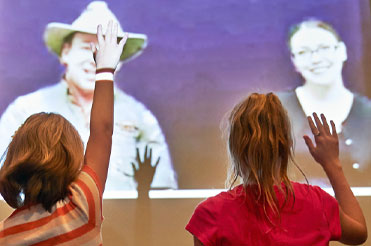two children sitting in front of a projected image of two teachers at Bullock Museum Distance Learning