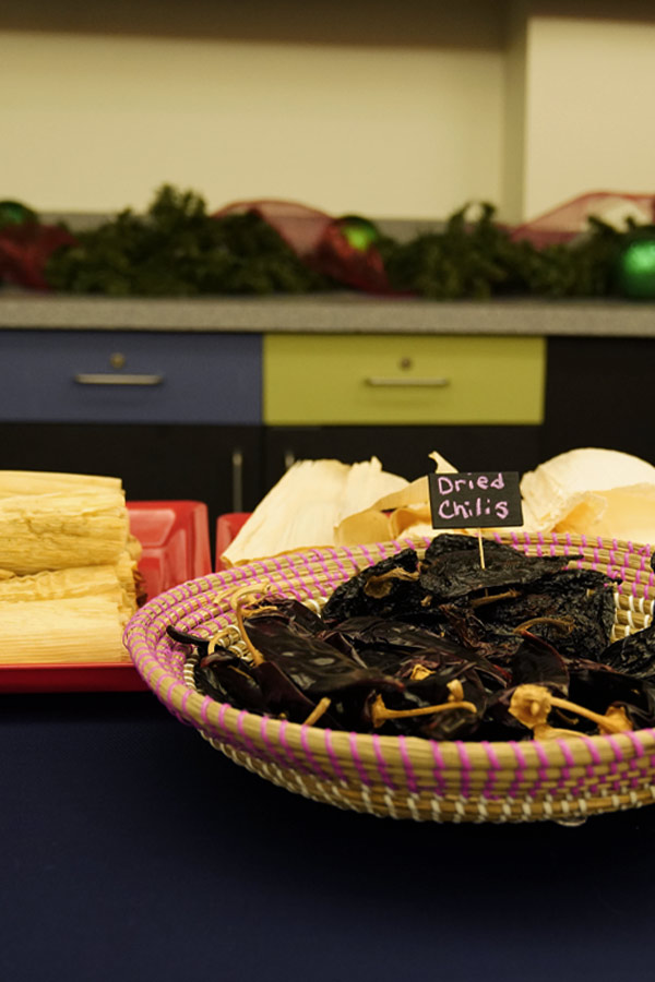A woven basket holding dried chilis next to tamale wrappers on a prep table.