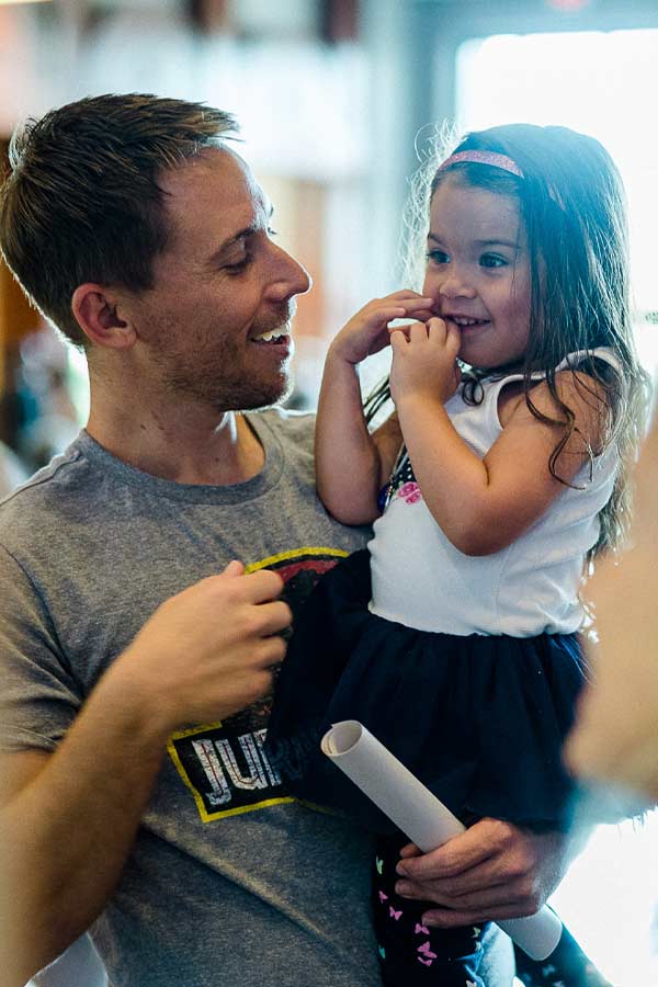 Man holding a young girl in his arms, they are looking at each other and smiling