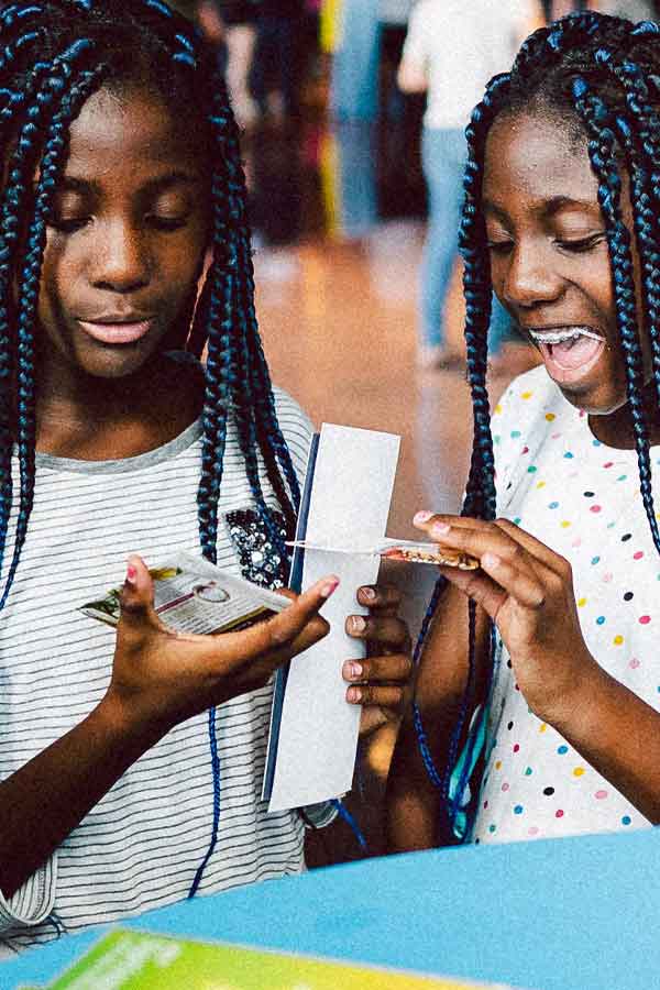 Two young girls standing at a table, holding activity guides and smiling