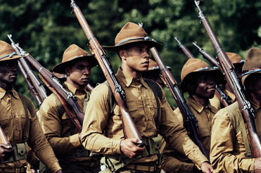 marching men in brown soldier uniforms, holding rifles on their shoulders