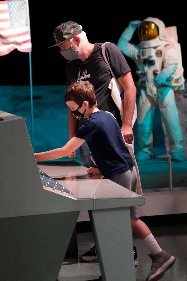 man and young boy wearing masks interacting with the mission control console at the Bullock Museum