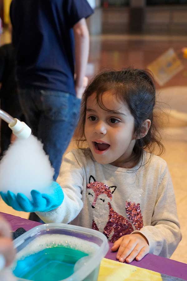 young girl with a big smile holding her hand out to catch fog from dry ice