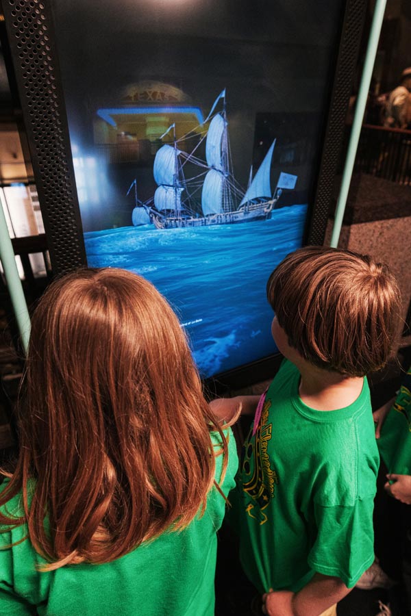 two children playing with a digital interactive with a rendering of a ship at the Bullock Museum.