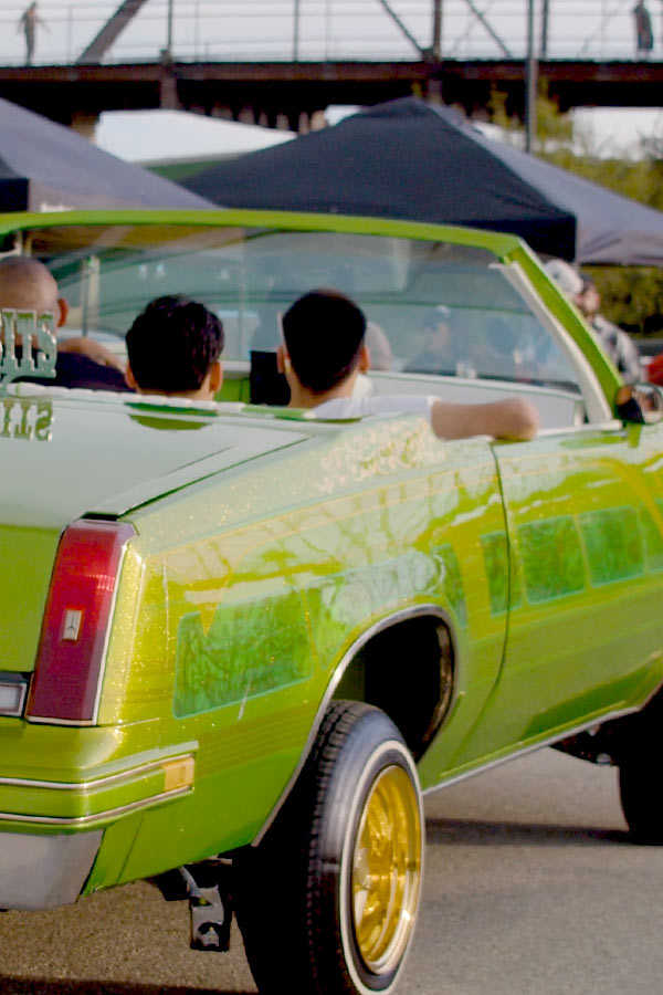 Three people sitting in a lime green lowrider car at an event.