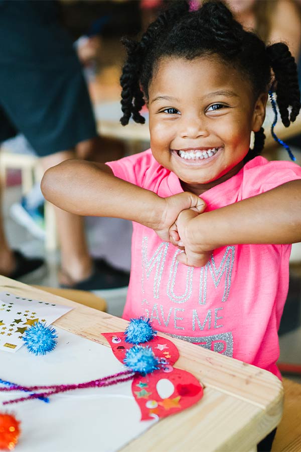 a young girl smiling and holding her hands together at a craft activity station in the Bullock Museum