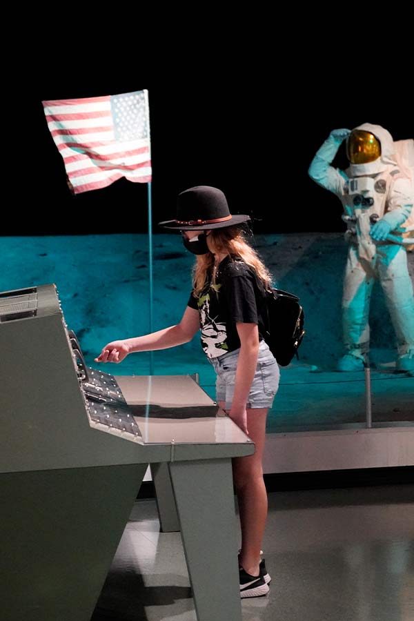 a girl pressing buttons on the mission control console in front of a statue of an astronaut in the Bullock Museum