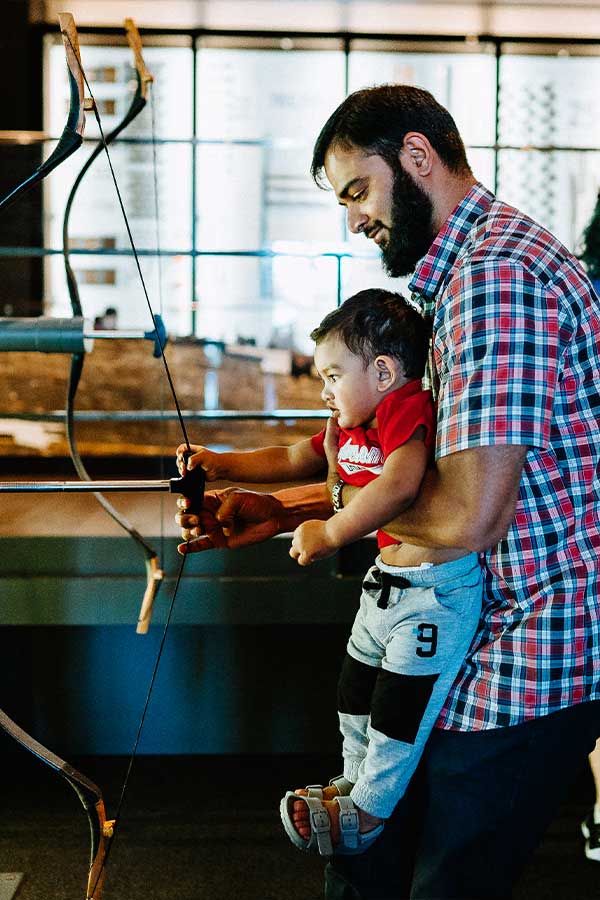 a man holding a child up to an interactive bow and arrow at the Bullock Museum