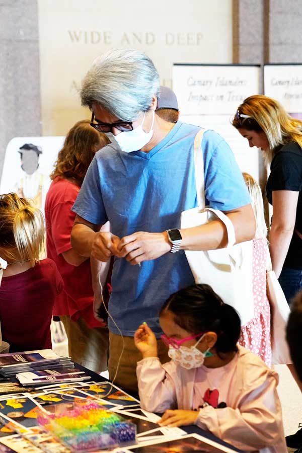 an adult and child putting beads on a string in the Bullock Museum