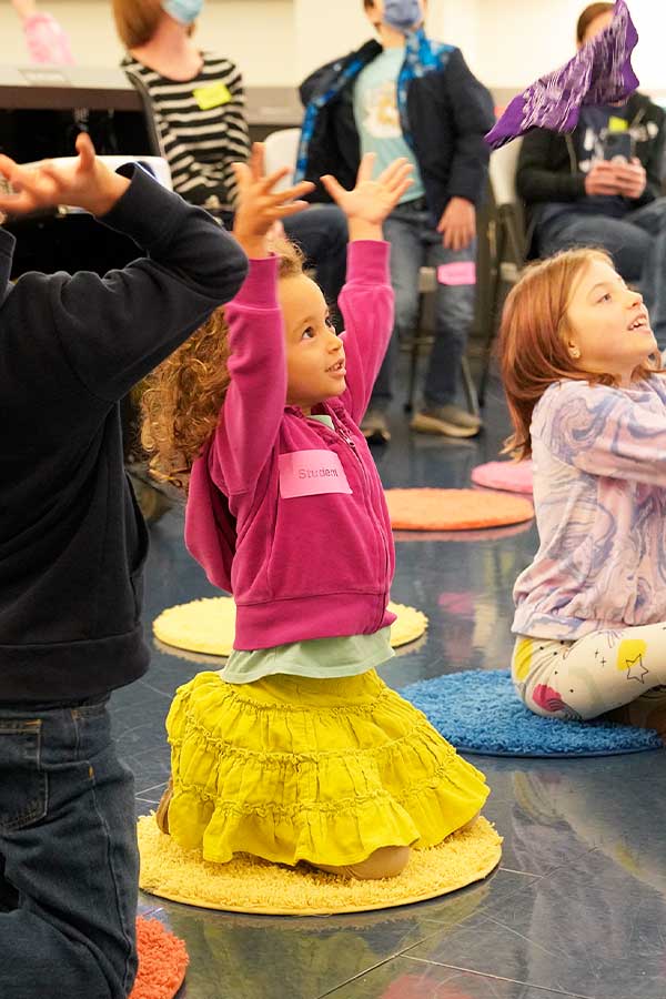 a young girl in a pink jacket raising her hands in the air as she participates in a story time activity
