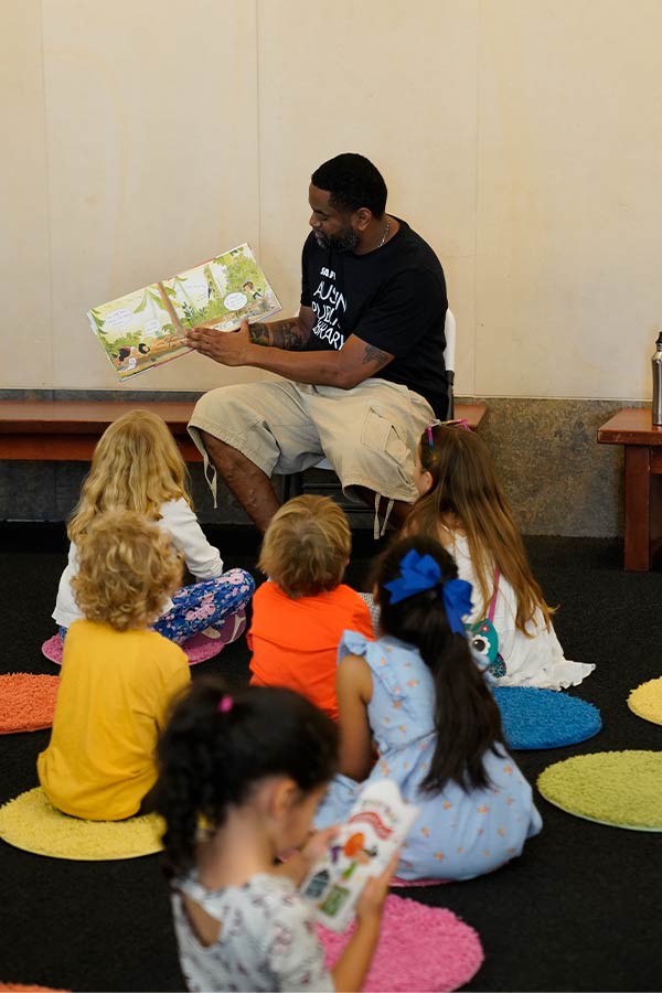 a group of kids sitting on the floor in front of a man reading a book at story time