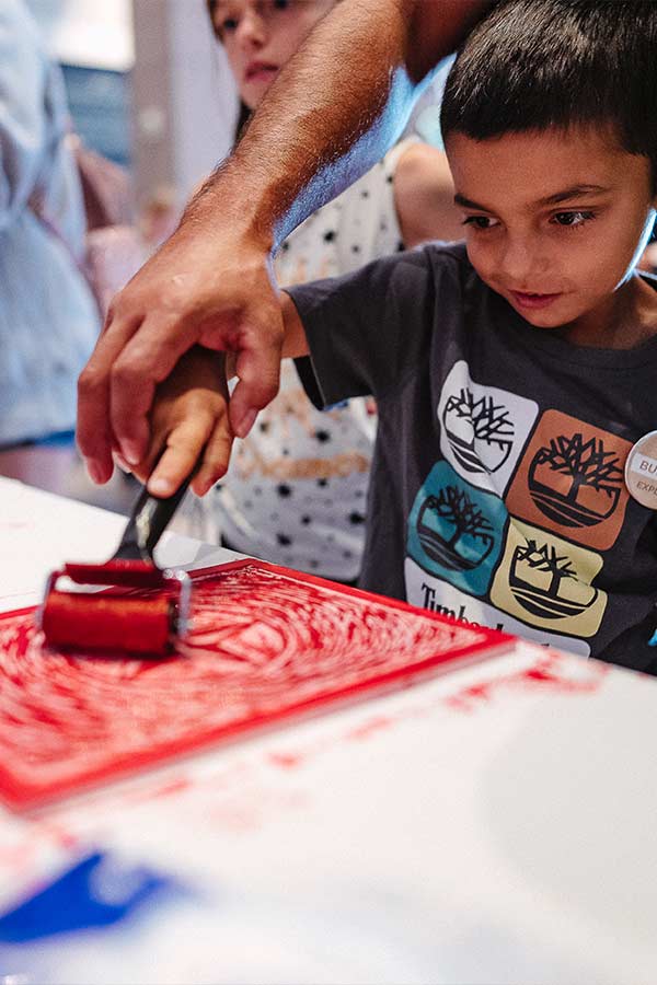 a child rolling red ink onto a print block in the Bullock Museum