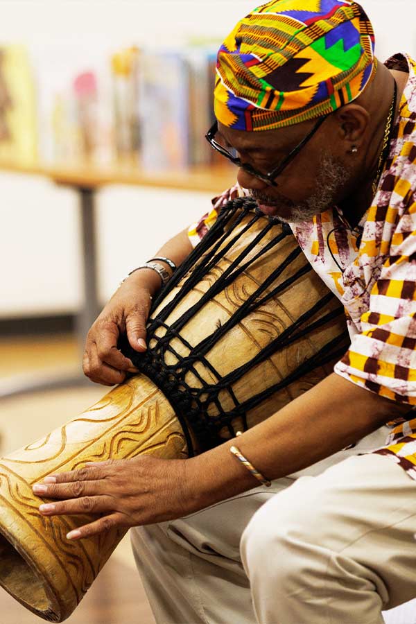 a Black man sitting down drumming while telling a story