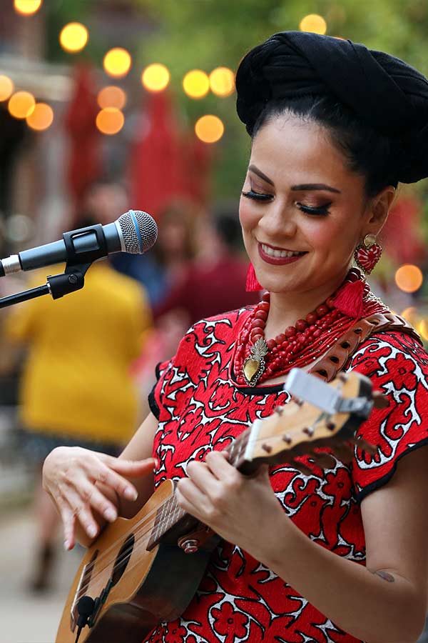 Azul Barrientos playing an acoustic guitar outside with a microphone