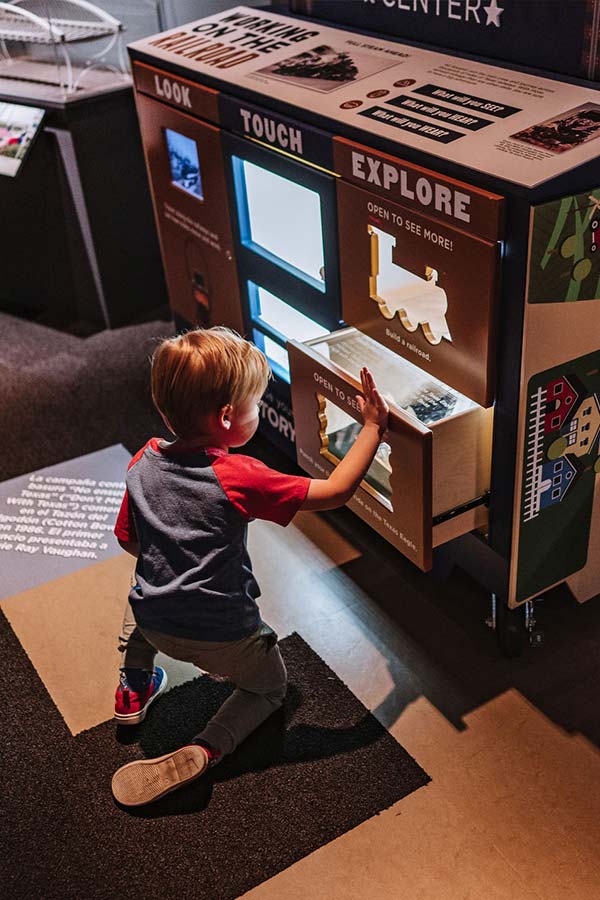 a young boy kneeling on the ground interacting with a learning cart in the Bullock Museum