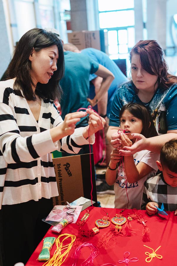 A person demonstrating a craft to a child and their caregiver.