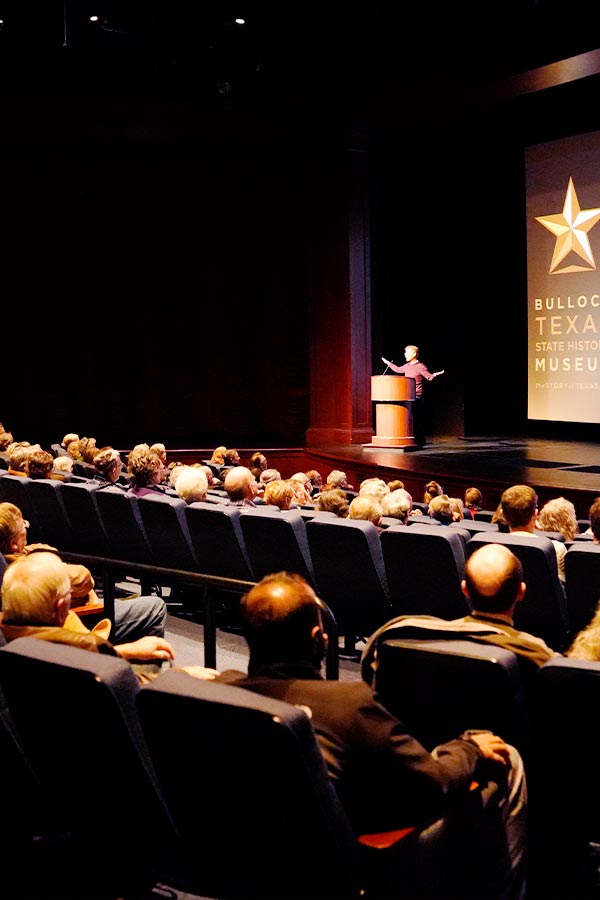 group of people sitting in the Texas Spirit Theater with a speaker at the podium in the Bullock Museum