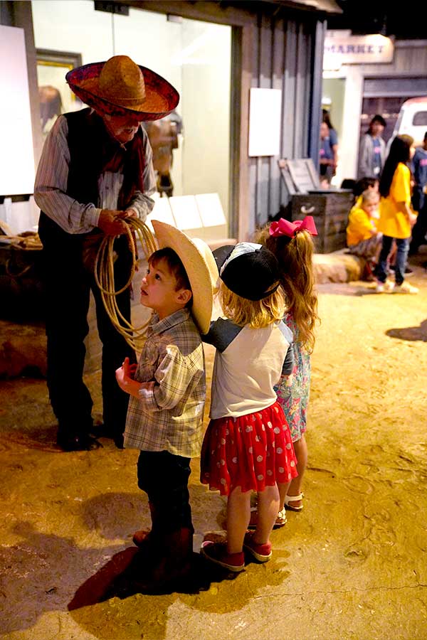 three small children in the Bullock Museum talking to a man in a cowboy outfit