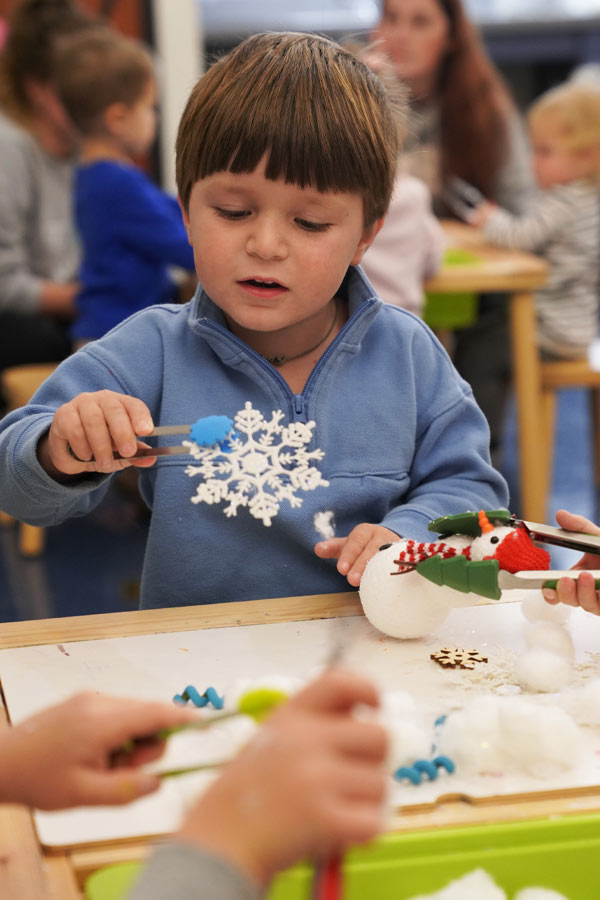 A child sitting at a craft table with a craft snowflake.