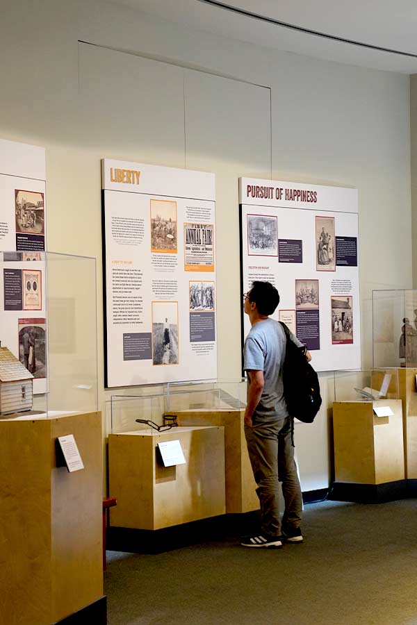 man standing in front of wall graphics and artifacts in the Black Citizenship in the Age of Jim Crow exhibit