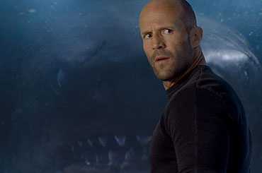 A man looks at the camera as a shark watches over his shoulder