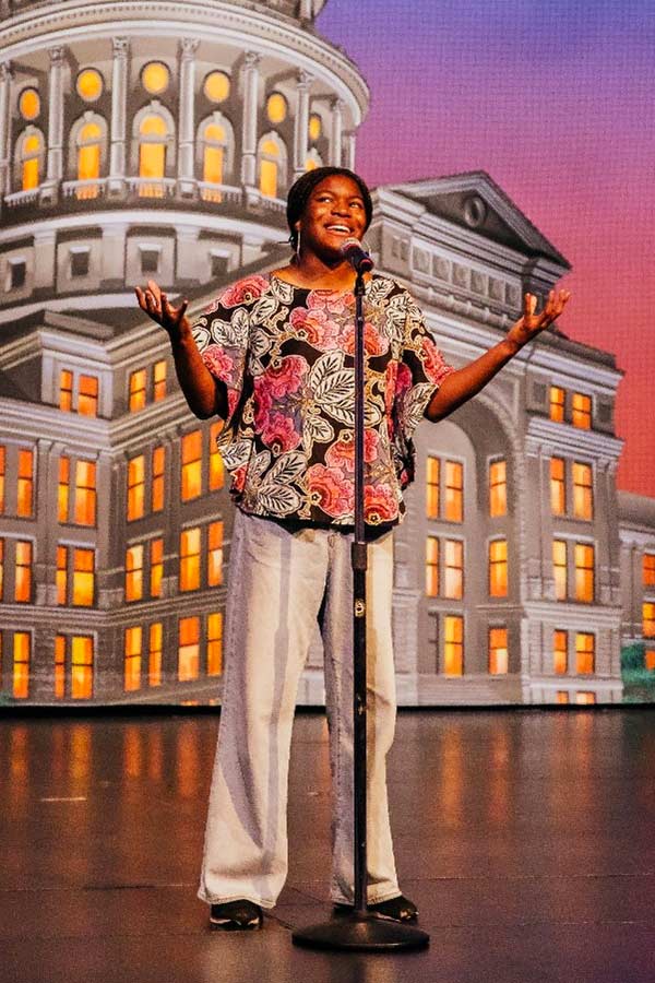 a Black woman on a stage in front of a microphone with the Texas Capitol in the background