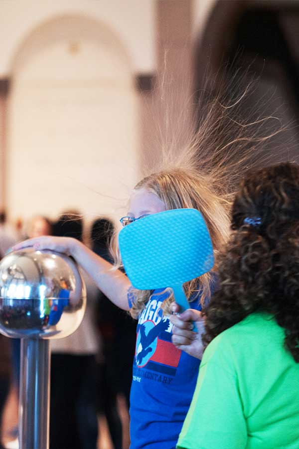 a young girl touching a Van Der Graff generator with her hair standing up