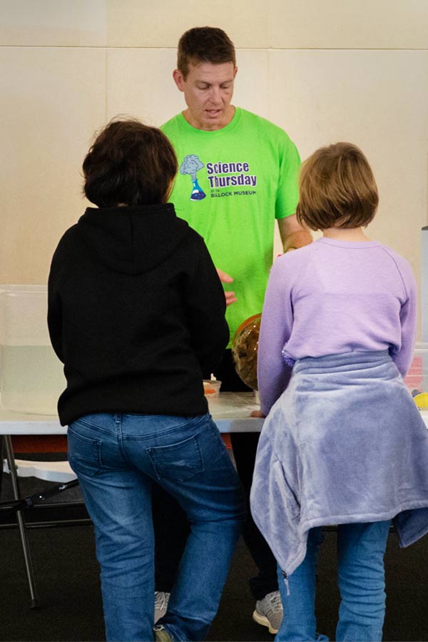 a man in a green shirt teaching two kids 