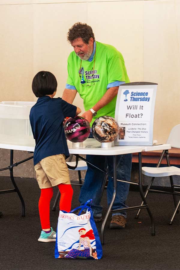 a man in a green shirt and a kid standing at a table with two bowling balls