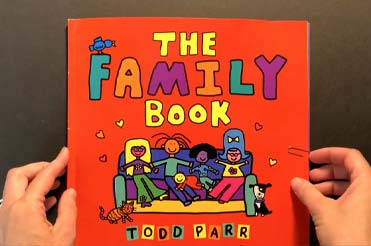 Two hands holding an orange book, the title reads "The Family Book, Todd Parr"