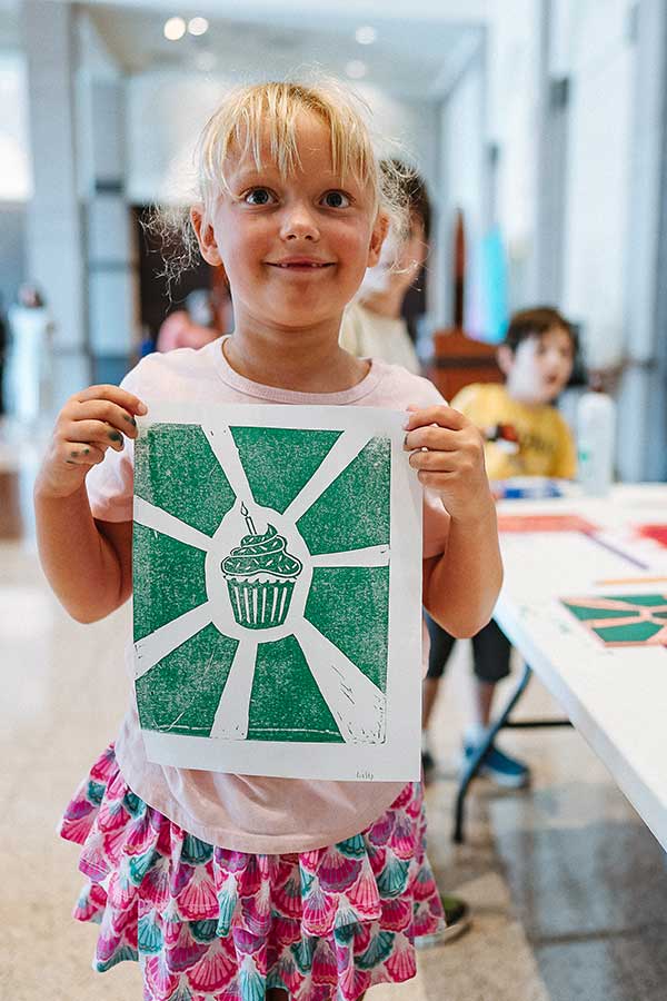 a young girl holding up a green block print of a cupcake
