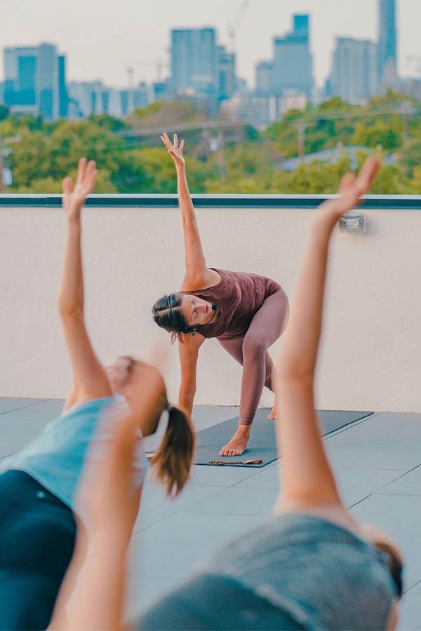 three adults doing yoga outside with a skyline in the background