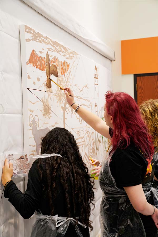 two teenagers, one with pink hair, working on a mural in the Bullock Museum