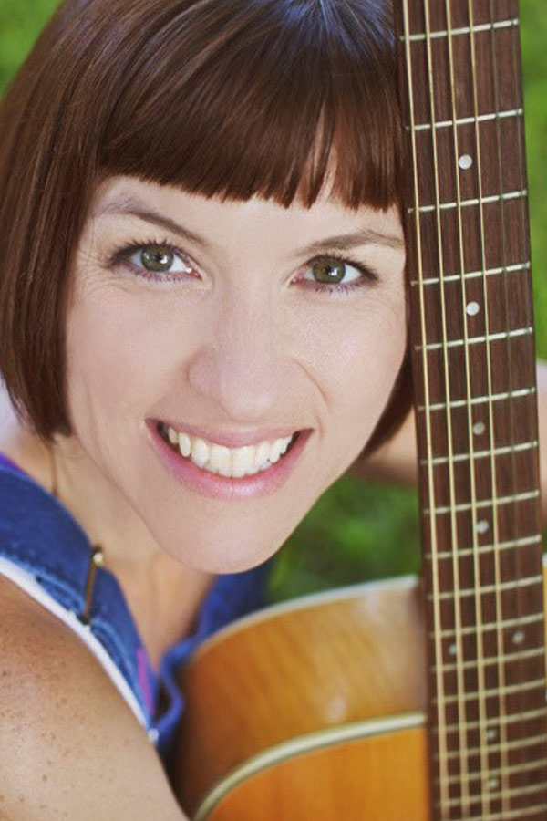 children's musician Staci Gray smiling, posing with an acoustic guitar