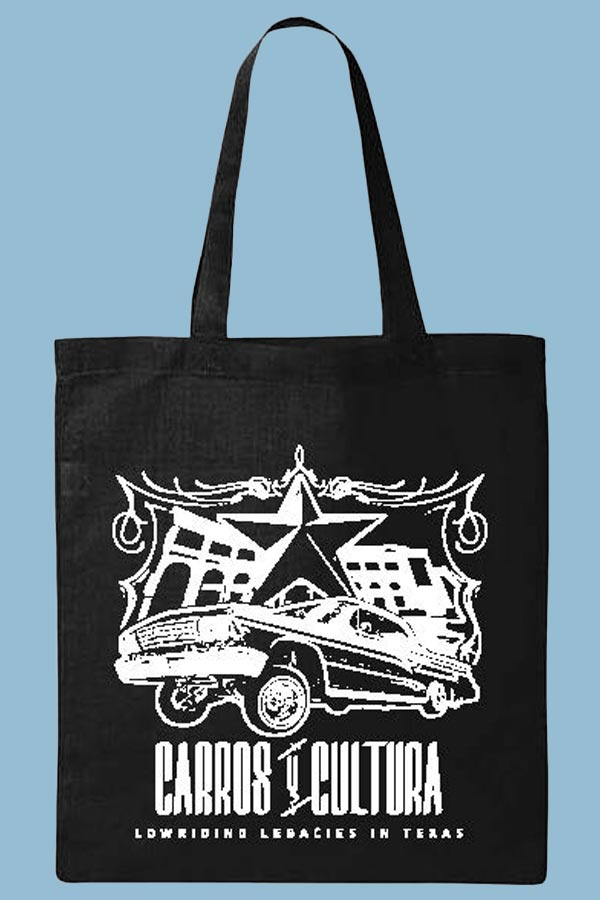 a black tote bag on top of a blue background, screen printed with the Carros y Cultura exhibit advertisement