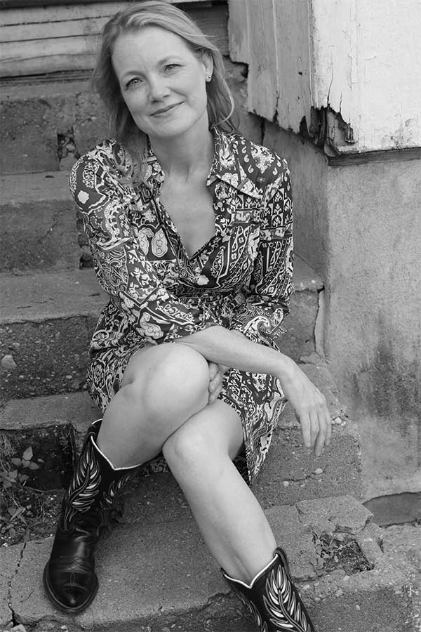 black and white photo of Kelly Willis sitting on steps with cowboy boots