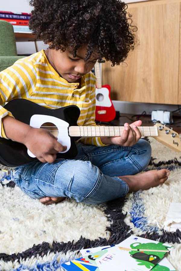 child sitting on the floor playing a black child's size guitar