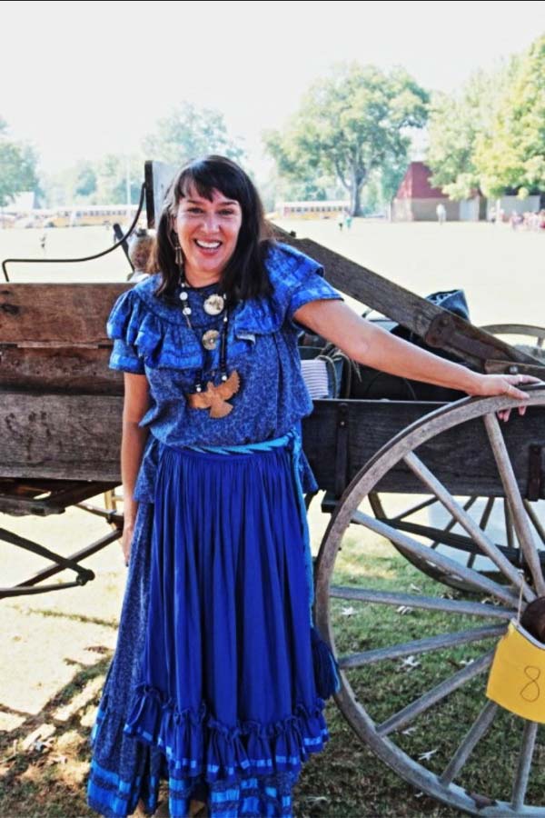 Woman in blue dress standing in front of a wooden cart