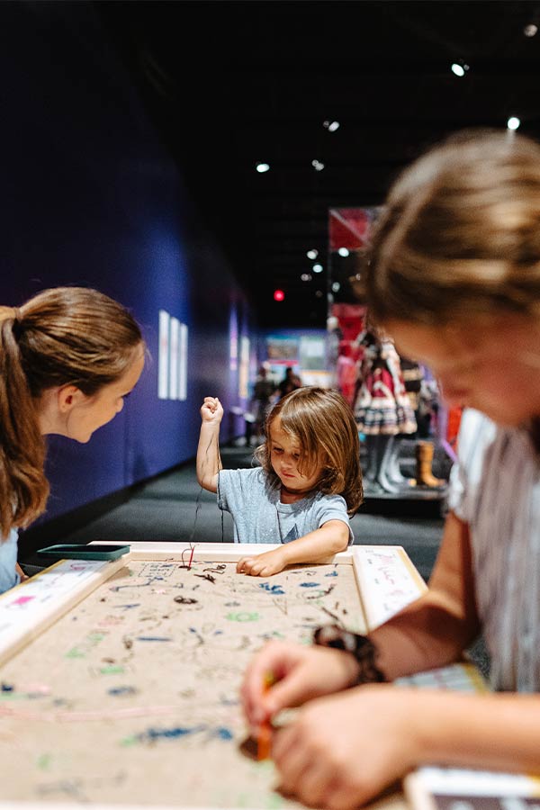 a young child pulling thread through a piece of burlap in the Bullock Museum