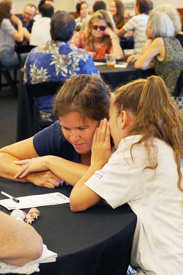 a young adult whispering to an adult while playing trivia