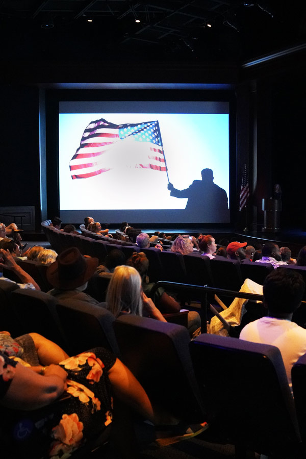 People watching a video with an American flag on a screen in a theater.